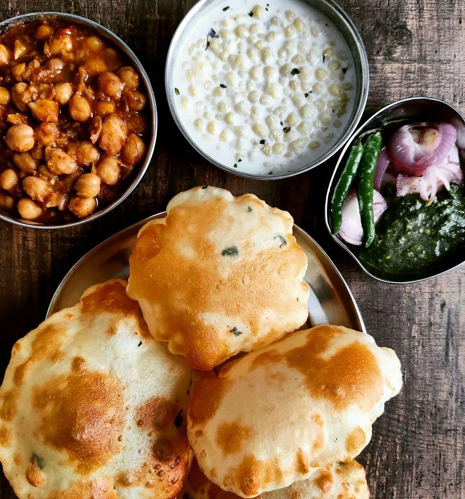 A warm wooden table topped with multiple bowls of nourishing Indian food.