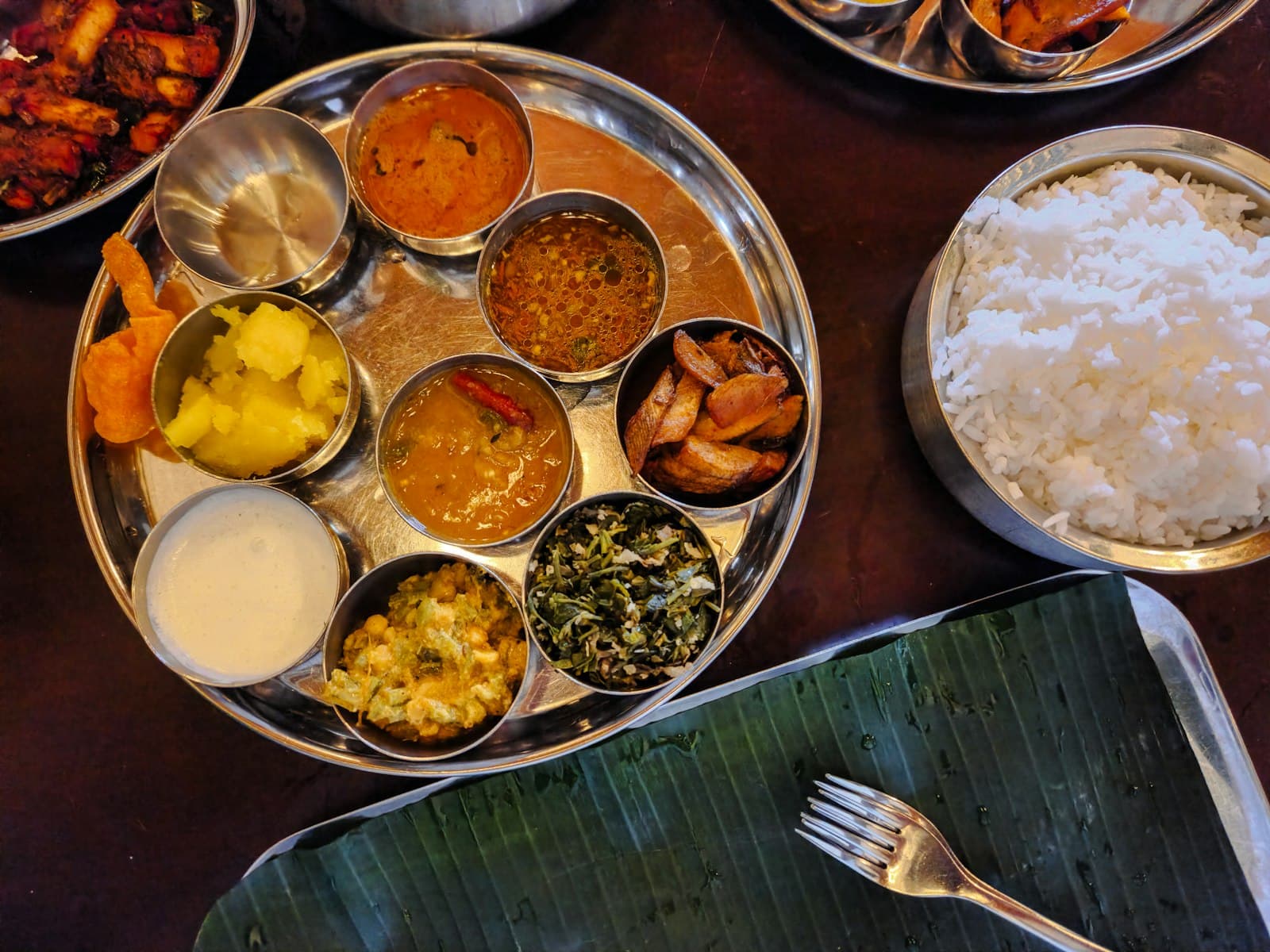 An overhead view of a full Indian thali with multiple side dishes — dal, sabzi, rice, raita — laid out on a table.
